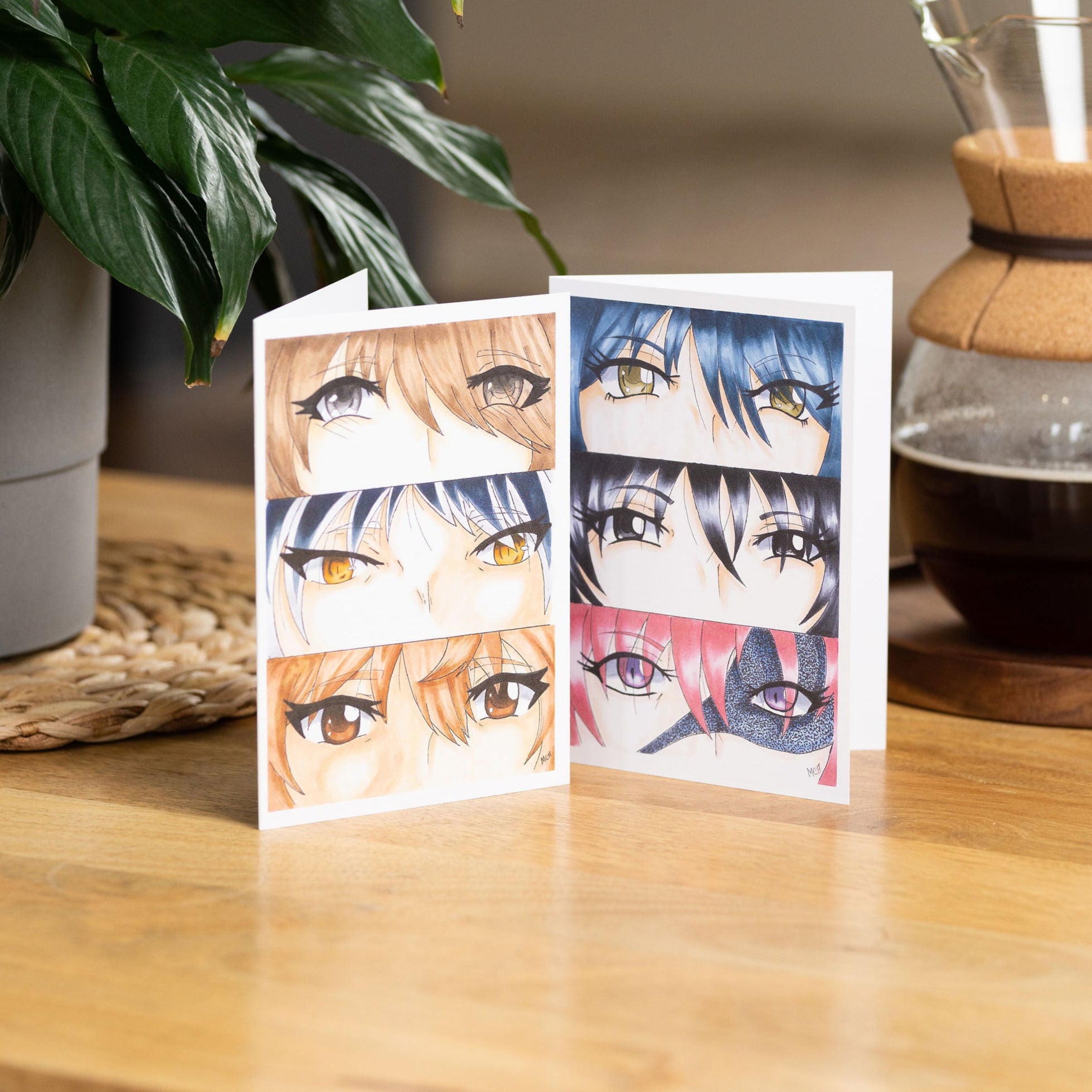 Girl's Eyes And Boy's Eyes A6 Greetings Cards On A Wooden Table With A Pot Of Coffee And A Potted Plant